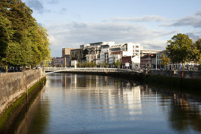 Arch bridge over river by buildings against sky, cork.