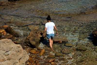 Rear view of woman standing on rock by sea