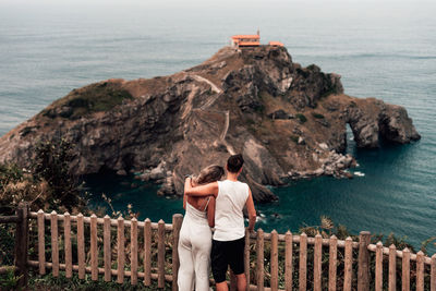 Rear view of couple standing by railing over sea