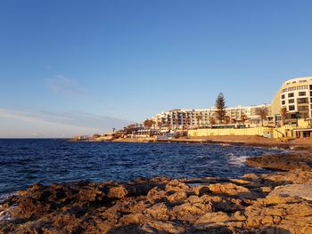 Sea by city buildings against clear sky