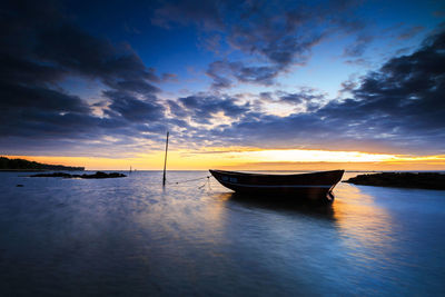 Boat moored on sea against sky during sunset