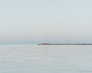 Lighthouse by sea against clear sky