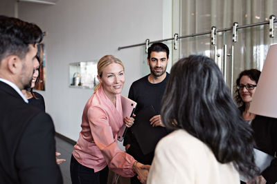 Businesswomen greeting while standing with colleagues in lobby at office