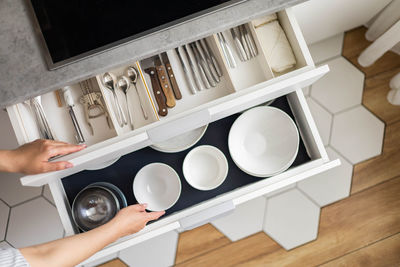 Cropped hands of woman arranging cutlery in cabinet