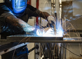 Unrecognizable male welder using welding machine on metal detail while working at workbench in factory