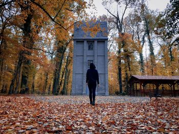 Rear view of woman in black hoodie standing in front of an old tower in the forest during autumn