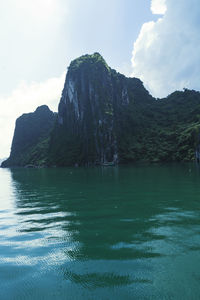 Scenic view of sea by mountain against sky