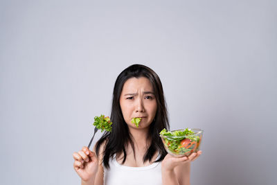 Portrait of young woman eating food against white background