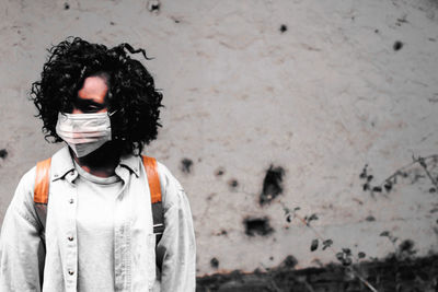 Woman wearing protective mask while standing against wall