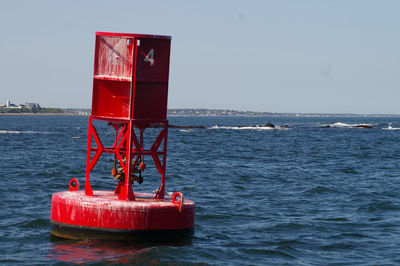 Red buoy floating on sea against clear sky