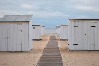 Huts at beach against cloudy sky