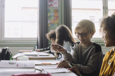 Smiling friends playing while sitting at desk in classroom