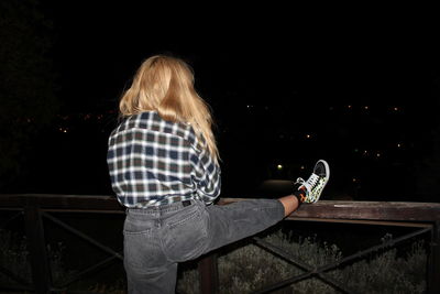 Rear view of woman standing against railing at night