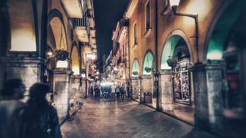 People walking on illuminated street amidst buildings in city at night