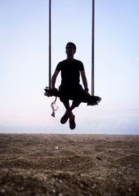 Full length portrait of man swinging against clear sky