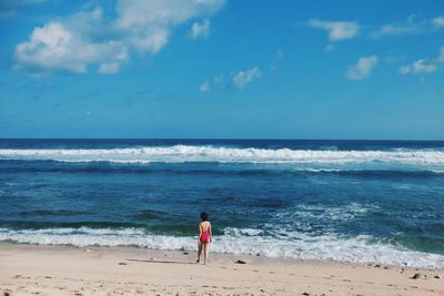 Rear view of woman standing at beach against sky