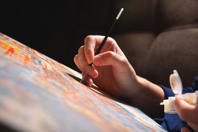Close-up of a female artist's hand painting with watercolors color on canvas with a brush in a dark