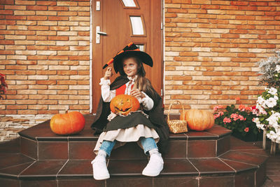 Portrait of smiling girl holding pumpkin against brick wall