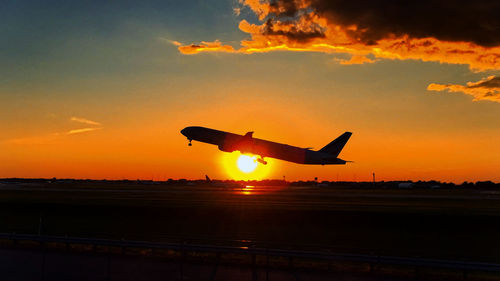 Low angle view of silhouette airplane flying against sky during sunset