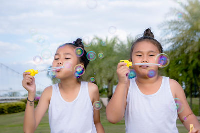 Siblings blowing bubbles against trees