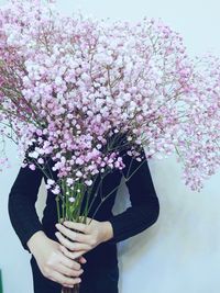 Person holding pink flowers against wall