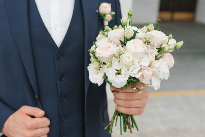 The groom in a blue suit holds in his hand a delicate wedding bouquet for his beloved bride