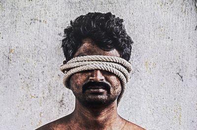 Close-up of shirtless mid adult man with rope rolled up on face