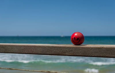 Red stress ball on wooden railing against sea