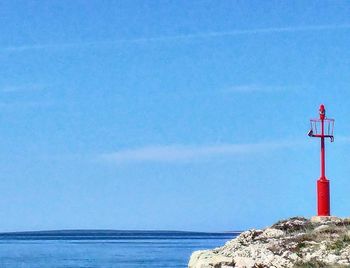 Lighthouse by sea against clear blue sky