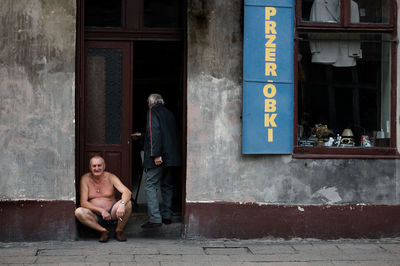 Man and woman sitting on street at entrance of building