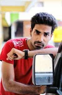 Portrait of man leaning on cropped car