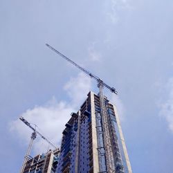 Low angle view of crane by incomplete buildings against sky
