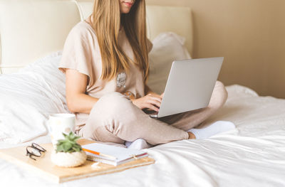 Low section of woman using laptop while sitting on bed at home