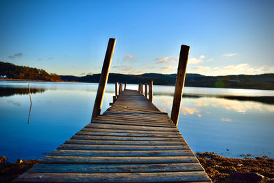 Wooden pier over lake against blue sky