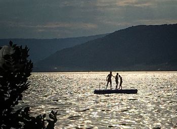 Silhouette men in lake against sky