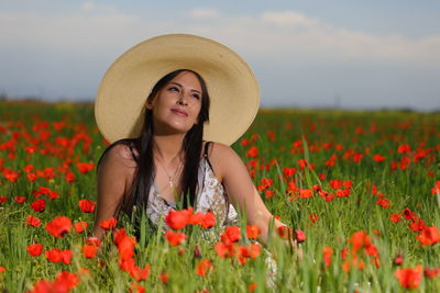 Portrait of beautiful young woman with red flowers in field