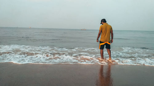 Rear view of man standing on beach against sky