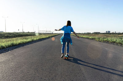 Skater young woman in blue jeans and t-shirt skateboarding on road in summer, active lifestyle