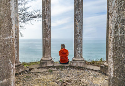 Rear view of man sitting by sea against sky