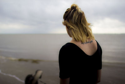 Rear view of woman standing at beach against sky