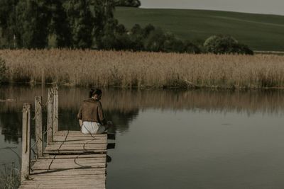 Rear view of woman sitting on pier at lake