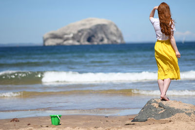 Rear view of woman on beach against sky