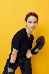 Portrait of young woman exercising against yellow background