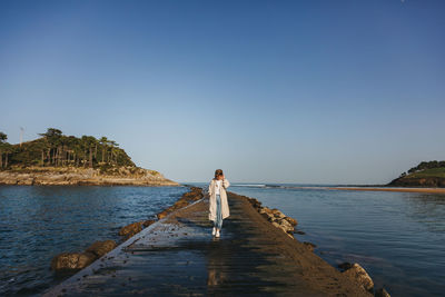 Rear view of woman standing on rock by sea against clear sky