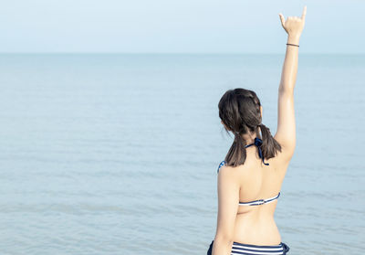 Rear view of woman with arms raised against sea
