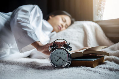 Woman touching alarm clock while sleeping on bed