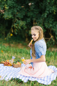 Pretty caucasian young woman with long hair is lsitting on a blanket in nature on a sunny summer day