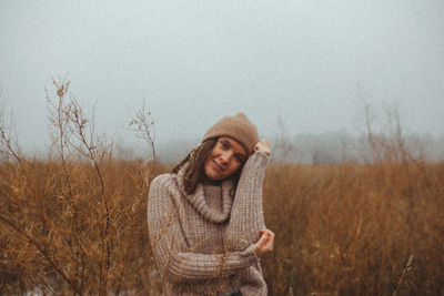 Woman wearing beanie on foggy field against sky during late autumn winter