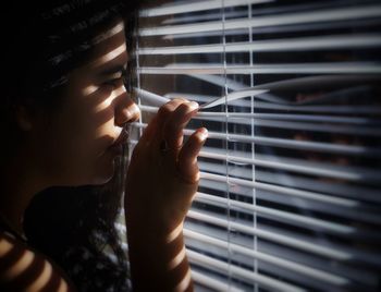 Close-up of woman looking through window blinds