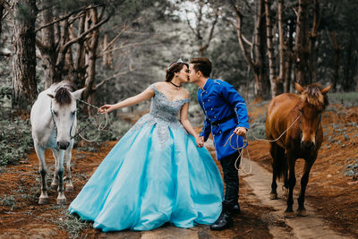 Wedding couple holding horses while kissing on mouth in forest